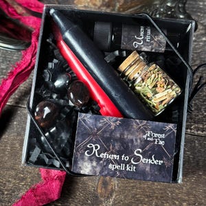 May include: A black box with a red candle, a small bottle of oil, a jar of herbs, and three black stones. The box has a label that says "Return to Sender spell kit" and "Forest and Fae".