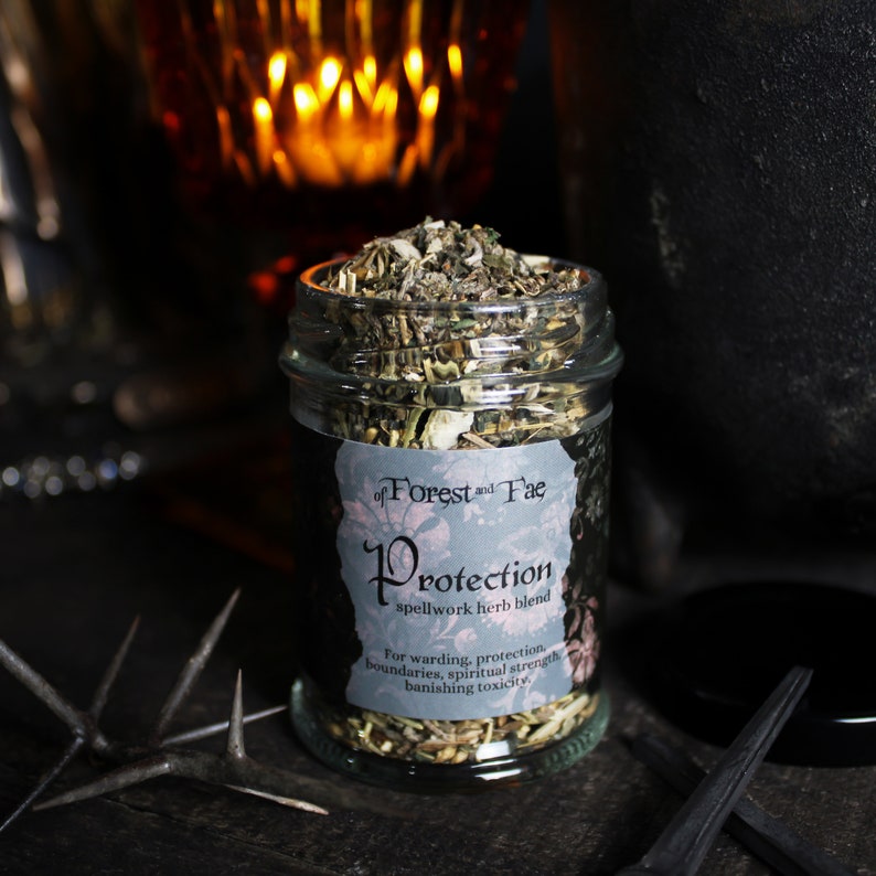 K&ouml;nnte beinhalten: Ein Glasgef&auml;&szlig; gef&uuml;llt mit getrockneten Kr&auml;utern, beschriftet mit "Protection spellwork herb blend" von "of Forest and Fae". Das Etikett besagt auch "F&uuml;r Schutz, Grenzen, spirituelle St&auml;rke, Beseitigung von Toxizit&auml;t."