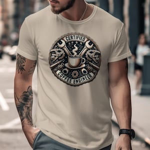 Puede incluir: Camiseta beige con un diseño circular que dice "CERTIFIED COFFEE ENGINEER". El diseño incluye una taza de café, llaves inglesas, engranajes y vapor. La camiseta es de manga corta y tiene cuello redondo.