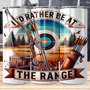 May include: A white tumbler with a design featuring archery equipment and the text "I'D RATHER BE AT THE RANGE." The design includes a bow, arrows, a target, and a leather quiver. The background shows a forest and a field.