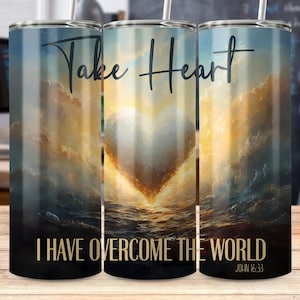 May include: A stainless steel tumbler with a blue and gold design featuring a heart shape and the words "Take Heart" and "I Have Overcome The World" with the scripture reference "John 16:33".