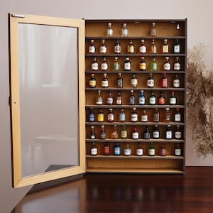 Op de afbeelding: Een houten vitrinekast met een glazen deur, gevuld met miniatuur drankflessen. De kast is open en toont rijen kleurrijke flessen. Hij staat op een donkerbruine houten tafel, met een neutraal gekleurde muur op de achtergrond.