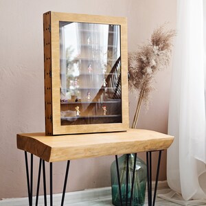 May include: A wooden display case with glass doors sits on a wooden table with black hairpin legs. The case is filled with small figurines.