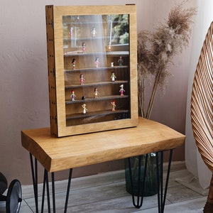May include: A wooden display case with glass doors and shelves, filled with small figurines. The case is sitting on a wooden table with black hairpin legs.