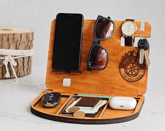 May include: A wooden desk organizer featuring a phone stand, a slot for sunglasses, a watch holder, and a key hook. The surface includes a laser-engraved compass design with the text EST. 2017 THE WILLIAMS. It has compartments for a car key, wallet, and earbuds.