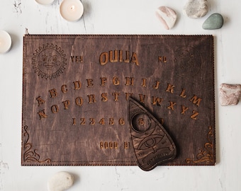 May include: A wooden Ouija board with a planchette. The board has a dark brown stain and features a traditional alphabet, numbers, and the words "yes", "no", and "goodbye".