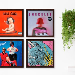 May include: Four framed vinyl records with different album covers. The top left album cover is red with the text "Papa Roach" in white. The top right album cover is pink with the text "Sherelle" in white. The bottom left album cover is blue with the text "Gossip" in white. The bottom right album cover is pink with a blue dragon and the text "Trident" in white.