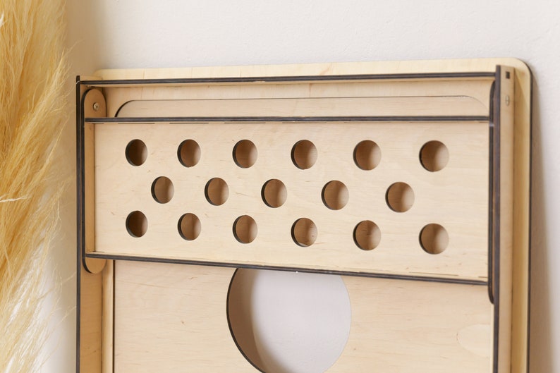 Puede incluir: Un organizador de pared de madera clara que cuenta con un estante rectangular con un panel frontal que contiene dos filas horizontales de recortes circulares. La estructura est&aacute; construida con l&aacute;minas de madera contrachapada con bordes oscuros.
