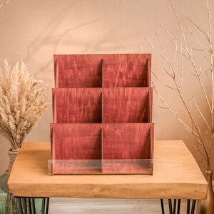 K&ouml;nnte beinhalten: Ein Holz-Pr&auml;sentationsst&auml;nder mit sechs F&auml;chern und einem transparenten Acryl-Regal. Der St&auml;nder ist aus dunkelrotem Holz gefertigt und eignet sich perfekt zum Pr&auml;sentieren von kleinen Gegenst&auml;nden.