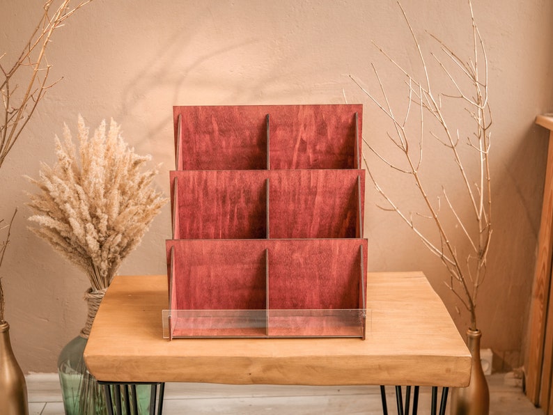 K&ouml;nnte beinhalten: Ein Holz-Pr&auml;sentationsst&auml;nder mit sechs F&auml;chern und einem transparenten Acryl-Regal. Der St&auml;nder ist aus dunkelrotem Holz gefertigt und eignet sich perfekt zum Pr&auml;sentieren von kleinen Gegenst&auml;nden.