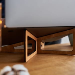 K&ouml;nnte beinhalten: Ein Laptop-St&auml;nder aus Holz mit nat&uuml;rlicher Holzoptik. Der St&auml;nder ist so konzipiert, dass er einen Laptop f&uuml;r bessere Ergonomie und Luftzirkulation anhebt.