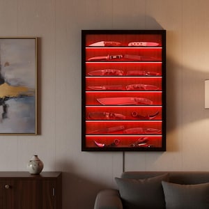 Op de afbeelding: Een rechthoekige wandvitrine met een donker frame en een achterpaneel met houtnerf, voorzien van acht horizontale planken verlicht door geïntegreerde rode ledverlichting, elk met diverse vouw- en vaststaande messen.