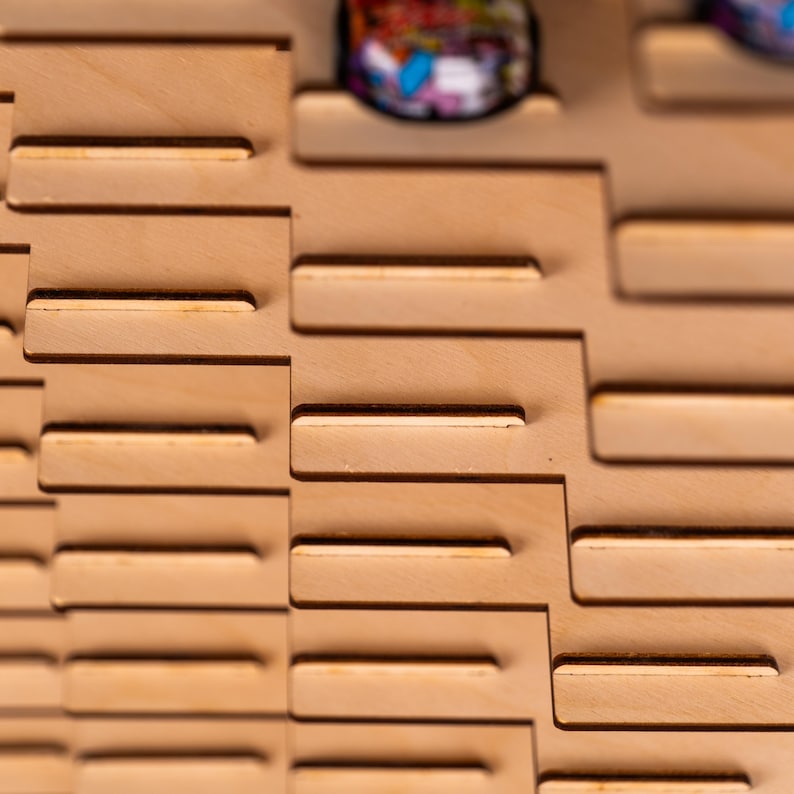 May include: A light-coloured wooden display rack featuring a stepped, interlocking design with horizontal slots. The structure is composed of flat, laser-cut panels arranged in a staggered pattern, creating multiple levels for holding small circular items.