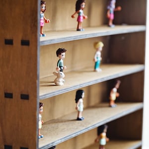 May include: A wooden shelf unit with five shelves, each displaying a small plastic figurine. The figurines are various colors and depict people and animals.