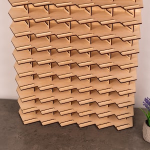 May include: A light-coloured wooden display stand featuring a repeating zigzag pattern with multiple horizontal shelves. The structure is composed of interlocking panels with a natural wood grain finish, designed with a series of small, evenly spaced ledges.