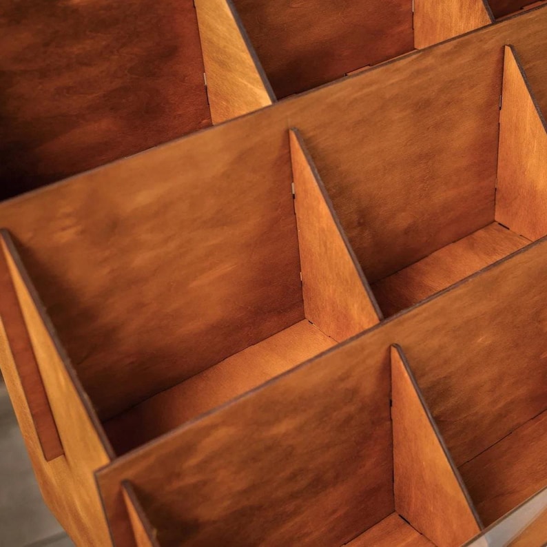Pu&ograve; includere: Un organizer in legno con pi&ugrave; scomparti. Gli scomparti sono divisi da divisori verticali e angolati, creando una struttura a griglia. Il legno ha una calda tinta marrone-rossastra e la costruzione appare robusta.