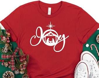 May include: Red t-shirt with a white design that says "Joy" with a star and a nativity scene inside a circle.