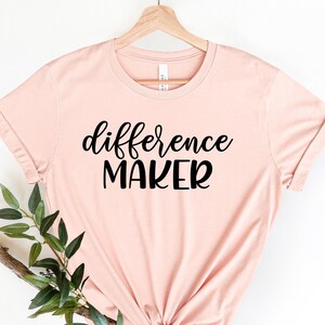 May include: A blush pink t-shirt with the text "difference maker" in black lettering.