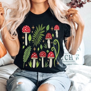 May include: A black t-shirt with a graphic print of red and white mushrooms, green leaves, and gold stars.