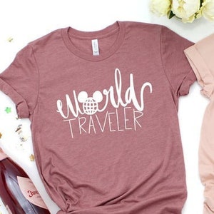 May include: Two t-shirts with the text "world traveler" and a Mickey Mouse head graphic. One shirt is pink and the other is a dusty rose color.