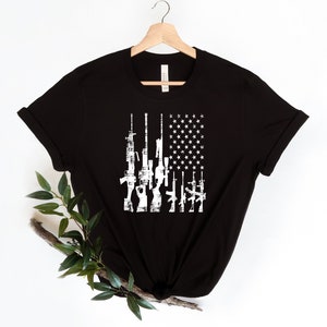 May include: Black t-shirt with a white distressed American flag design featuring a row of guns.