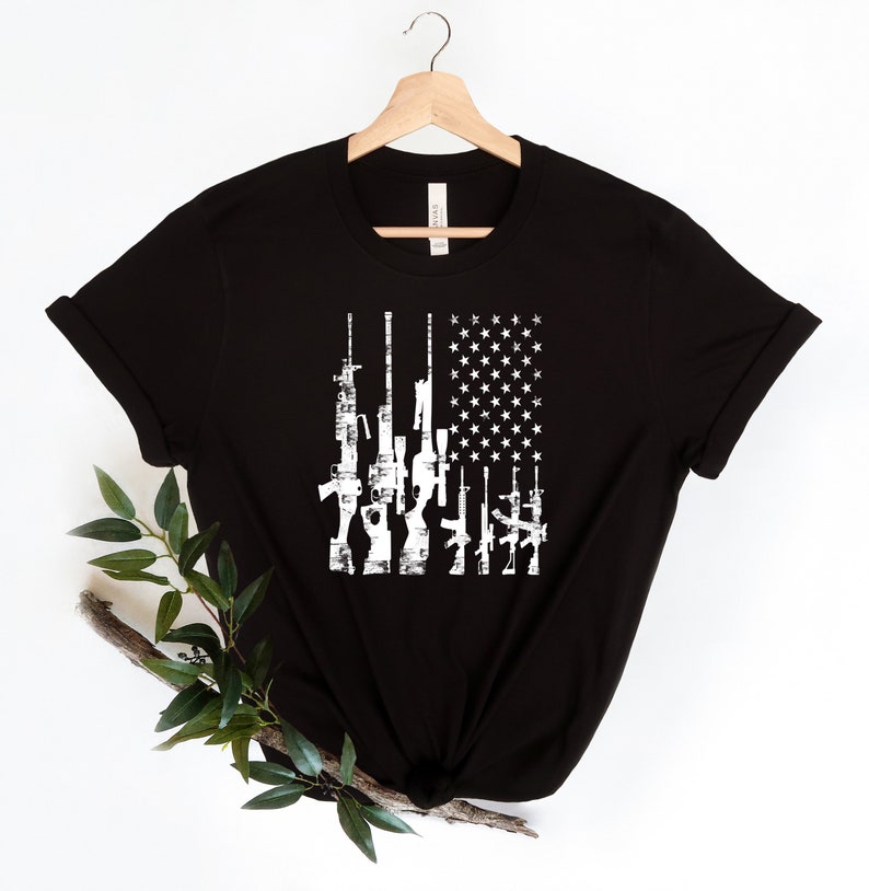 May include: Black t-shirt with a white distressed American flag design featuring a row of guns.