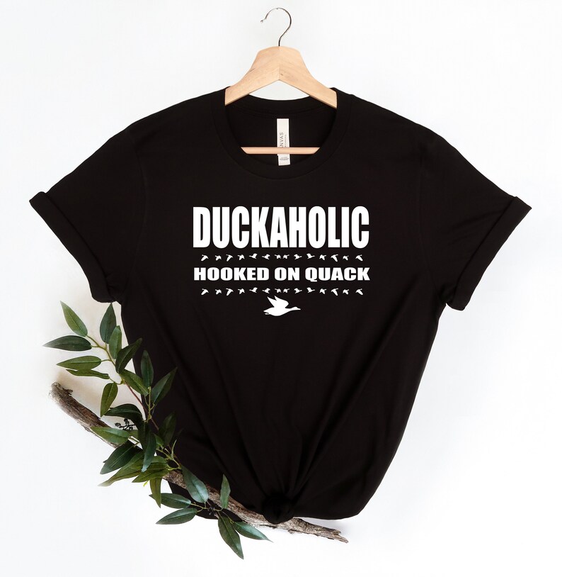 May include: Black t-shirt with white text that reads "Duckaholic Hooked on Quack" and a white silhouette of a duck.