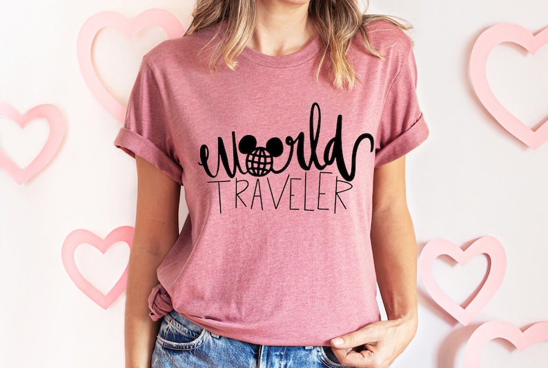 May include: A pink t-shirt with a black graphic that says "world traveler" with a Mickey Mouse head and a globe inside the ears.