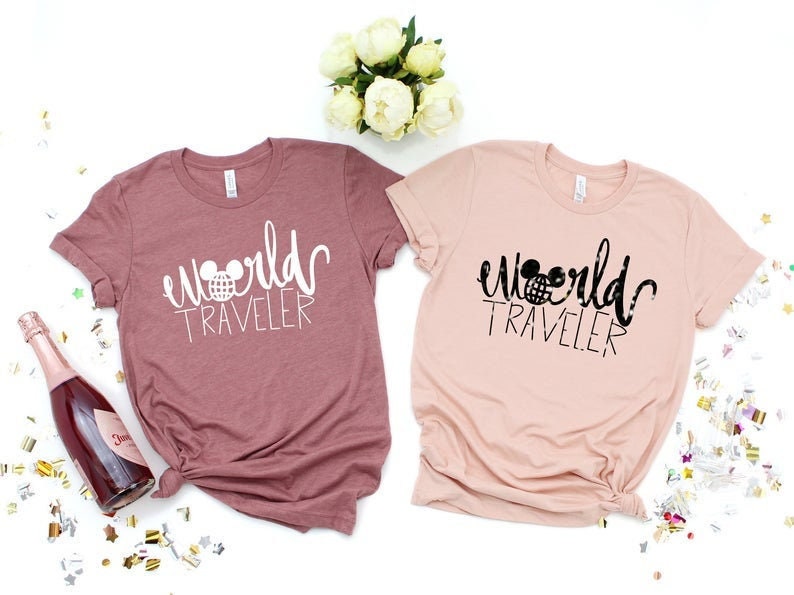 May include: Two t-shirts with the text "world traveler" and a Mickey Mouse head graphic. One shirt is pink and the other is a dusty rose color.