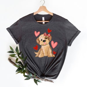 May include: A dark gray t-shirt with a cartoon illustration of a brown dog wearing a red bow with white polka dots. The dog is surrounded by pink hearts.