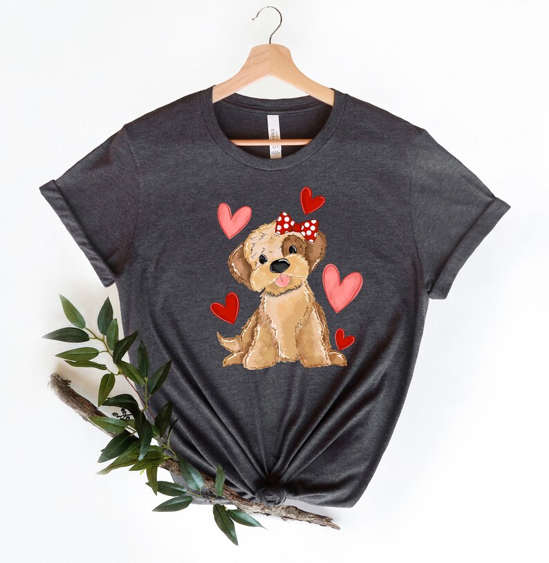 May include: A dark gray t-shirt with a cartoon illustration of a brown dog wearing a red bow with white polka dots. The dog is surrounded by pink hearts.
