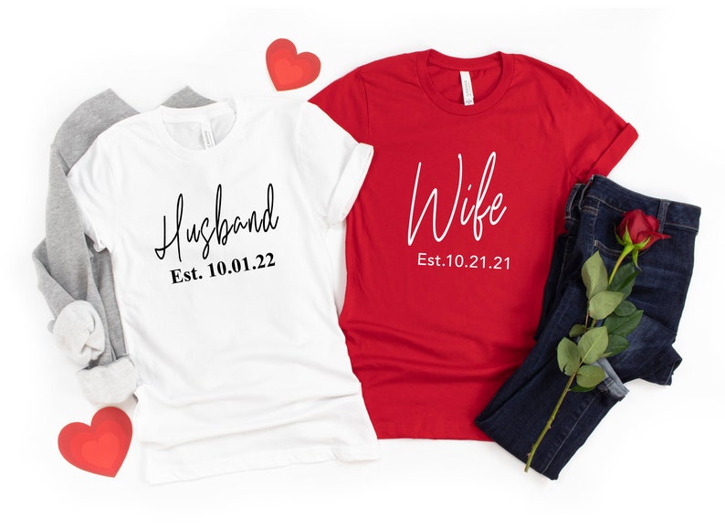 May include: Two white t-shirts with black text. One says "Husband Est. 10.01.22" and the other says "Wife Est. 10.21.21".