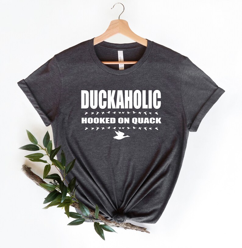 May include: A dark gray t-shirt with white text that reads "Duckaholic Hooked on Quack" and a white silhouette of a duck.