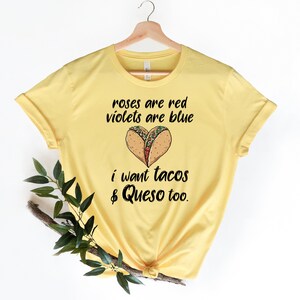 Op de afbeelding: Geel T-shirt met een grappige uitspraak over taco's en queso. De tekst luidt "Roses are red, violets are blue, I want tacos & queso too."