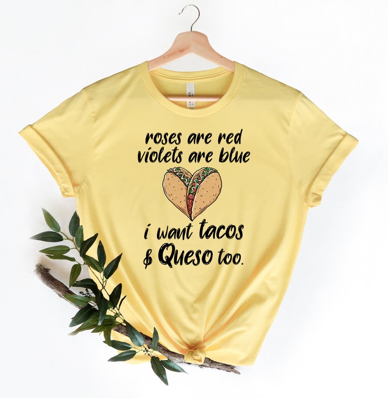 Op de afbeelding: Geel T-shirt met een grappige uitspraak over taco's en queso. De tekst luidt "Roses are red, violets are blue, I want tacos & queso too."