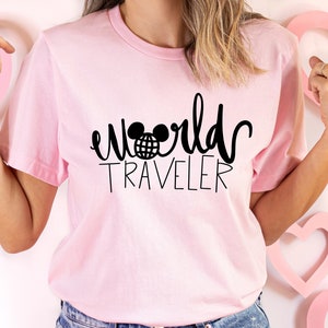 May include: Pink t-shirt with black text that says "world traveler" with a Mickey Mouse head and globe graphic.