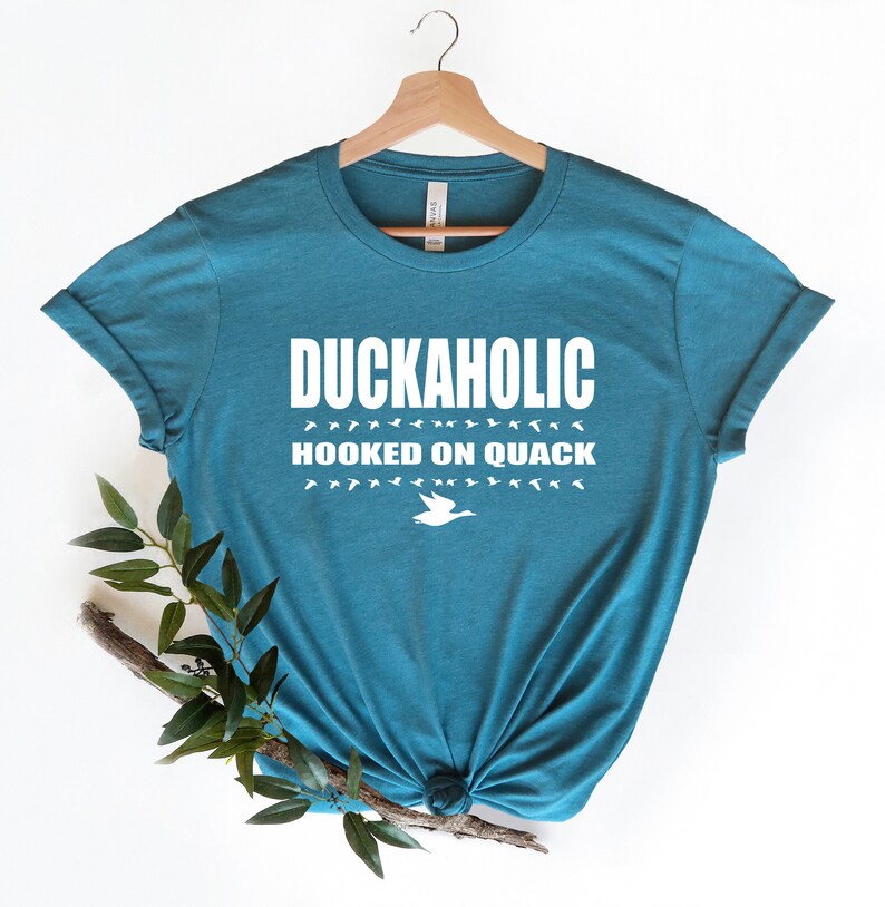 May include: Teal blue t-shirt with white text that reads "Duckaholic Hooked on Quack" and a white silhouette of a duck.