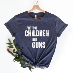 May include: A navy blue t-shirt with the text "PROTECT CHILDREN NOT GUNS" printed in white on the front.