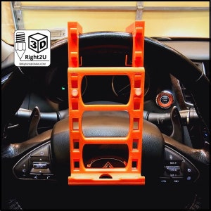 May include: Orange 3D printed phone holder for a car steering wheel. The holder has three slots to hold a phone in place.