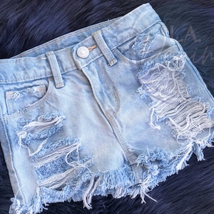 May include: Light blue denim shorts with frayed edges and multiple distressed holes. The shorts have a button and zipper closure.
