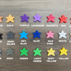 May include: A collection of 15 star-shaped buttons in various colours, including copper, gold, purple, lavender, magenta, red, orange, black, dark silver, sky blue, blue, silk pink, white, clear, silver, grey, green, light green, baby yellow, and yellow.