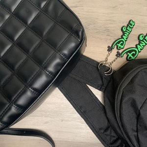 May include: Two black bags with green and purple name tags attached. The name tags read "Daniele" and "Liz".