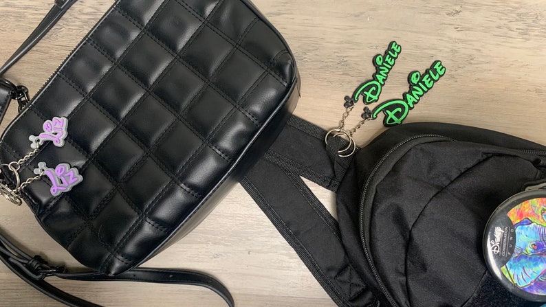 May include: Two black bags with green and purple name tags attached. The name tags read "Daniele" and "Liz".