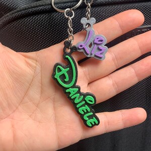 May include: A green and black keychain with the name "Daniele" and a purple and silver charm with the text "02".