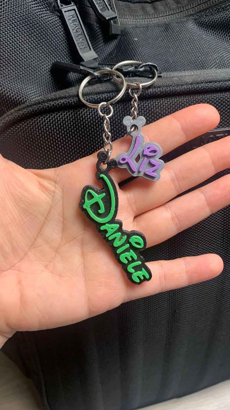 May include: A green and black keychain with the name "Daniele" and a purple and silver charm with the text "02".
