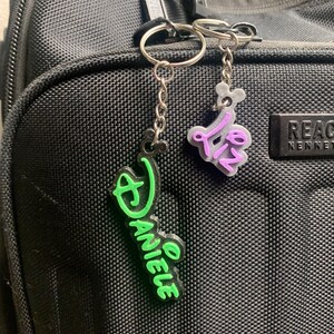 May include: Two keychains with personalised names. The keychain on the left is green and says "Danielle". The keychain on the right is purple and says "Liz".