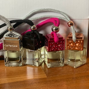 May include: Four small glass bottles with different colored metal caps and a decorative design. Each bottle has a string attached to the cap, and the text "Car Perfume" is printed on the front of one bottle.