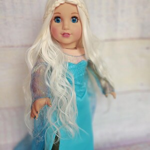 May include: A doll with long, white, wavy hair wearing a blue dress with a sparkly bodice. The doll has blue eyes and a light pink blush.