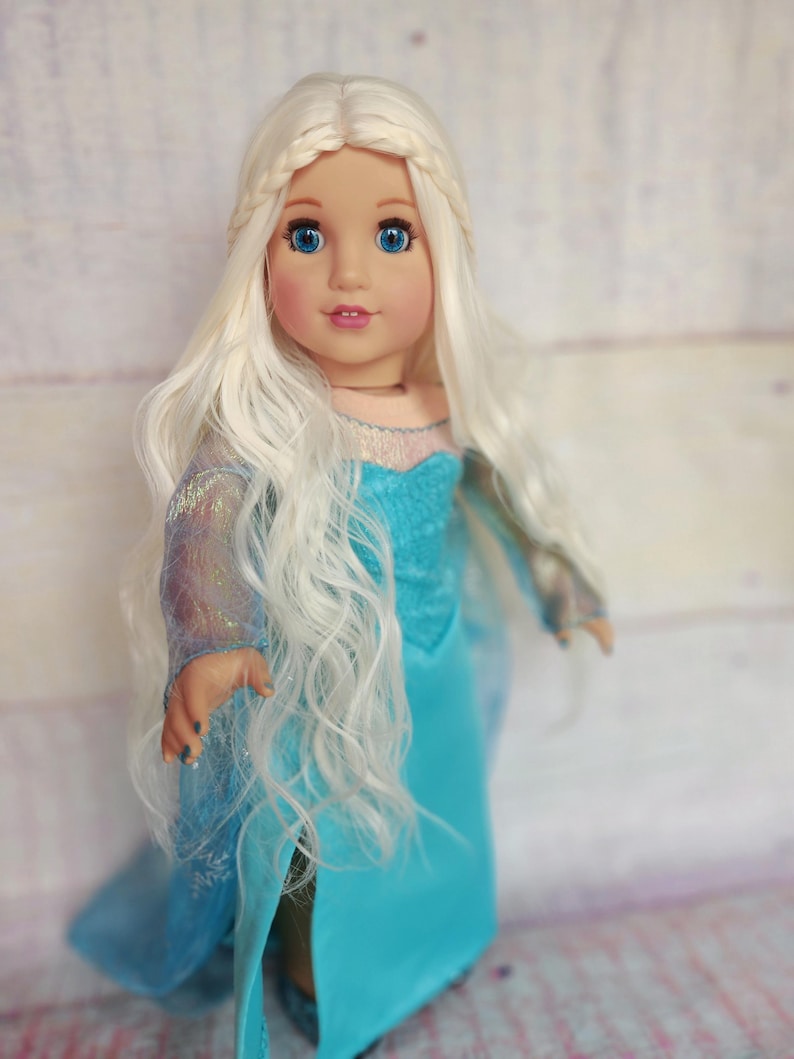 May include: A doll with long, white, wavy hair wearing a blue dress with a sparkly bodice. The doll has blue eyes and a light pink blush.