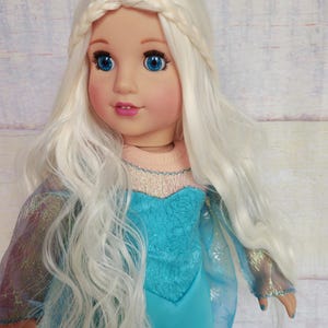 May include: A doll with long, white, wavy hair styled in a braid. The doll is wearing a blue dress with a sparkly bodice and a sheer overlay.